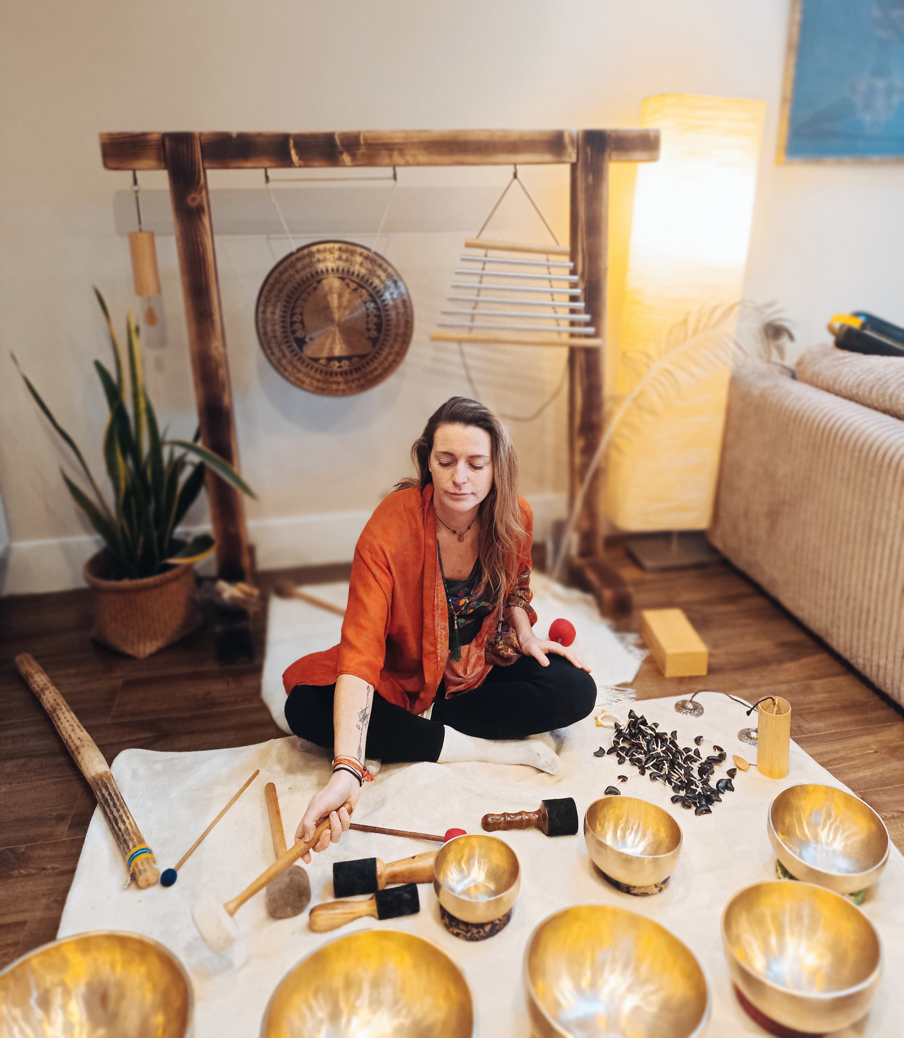 A sound healing therapist surrounded by instruments and playing himalayan bowls.