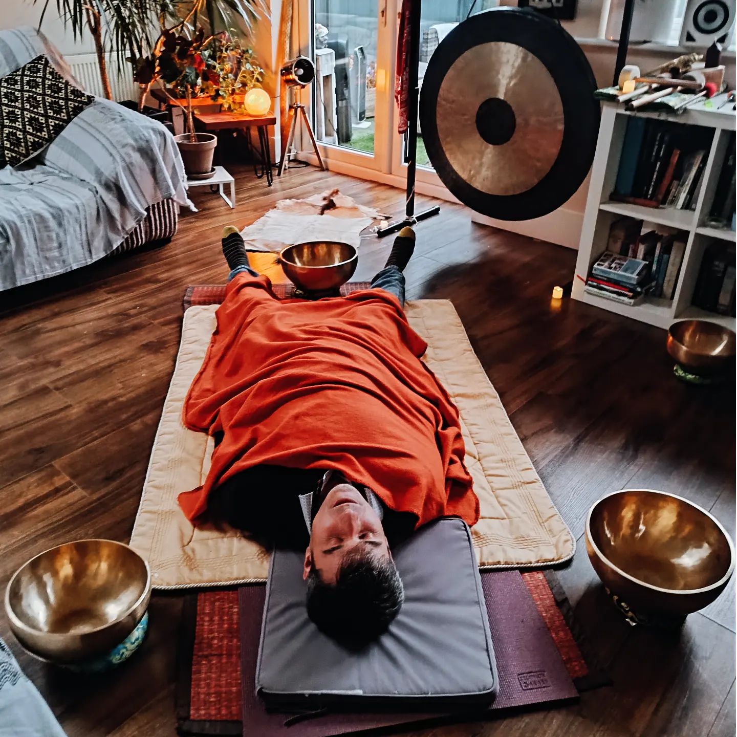 A man relaxing in a sound healing session, surrounded by himalayan bowls.