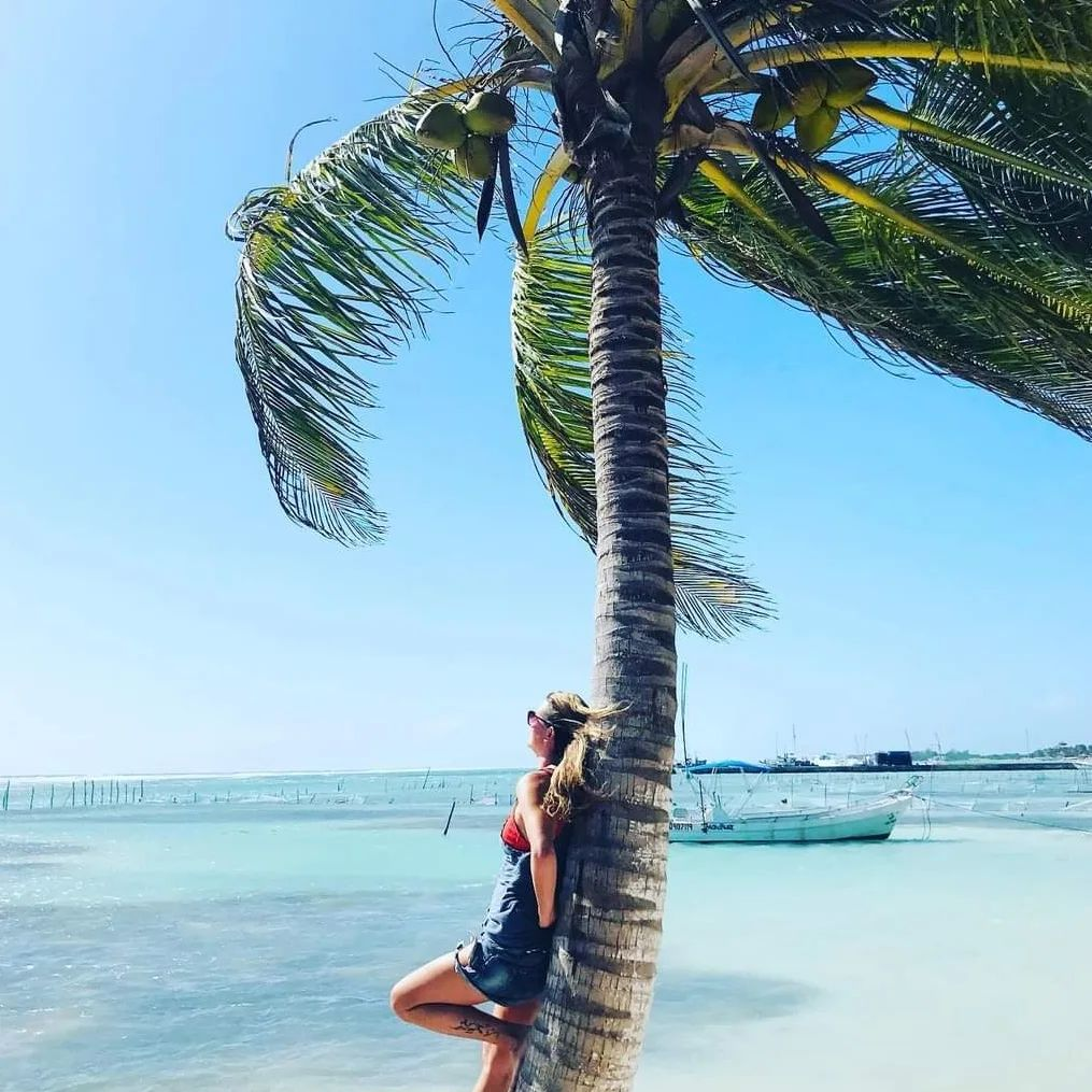 A sound healing therapist relaxing in the beach, leaning back on an palm tree.